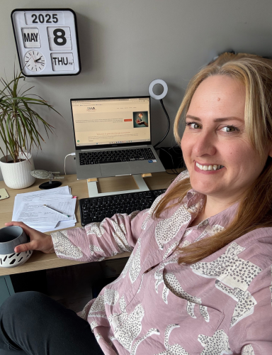 Me at my desk – May 2025 A photograph of a smiling woman in a pink shirt sat at her desk - it's me! On the desk is my laptop, open to my website homepage, a plant and a model of the USS Enterprise from Star Trek. I'm holding my mug of coffee, smiling into the camera.